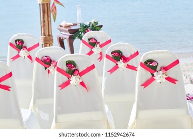 Back Side Of A Group Of White Spandex Wedding Chairs Cover With Red Pink Organza Sash For Beach Wedding Venue Settings