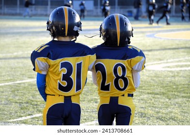 Back side of jerseys of 2 youth football players boys wearing helmets. Football field background #'s 31  28. Fall chilly morning. - Powered by Shutterstock