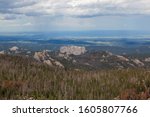 The back side of the large rock formation that is Mount Rushmore on the left with a parking area on the far right as seen from Black Elk Peak in Custer State Park, South Dakota.