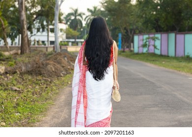 Back side of a pretty Indian woman in red saree and long hair walking on road