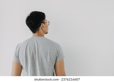 Back side, rear view of Asian man wear grey, haircut done. standing and thinking something, choosing and looking at empty space right side, isolated on white background wall.