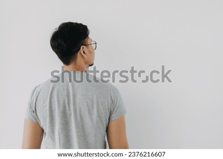 Back side, rear view of Asian man wear grey, haircut done. standing and thinking something, choosing and looking at empty space right side, isolated on white background wall.