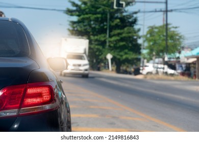 Back Side Of Sedarn Car Black Color On The Asphalt Road. With Traffic Conditions And Hot Sun During The Day And Other Cars Driving Opposite Lens.