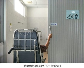 Back Side View Of Elderly Woman On Wheelchair Opening Sliding Door To Use The Bathroom In Hospital 