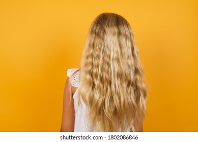 The Back Side View Of A Girl With Long Straight Wavy And Shiny Hair Standing Against Yellow Wall. Studio Shoot.