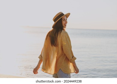 Back side view happy young woman 20s in straw hat shirt summer casual clothes standing look aside resting outdoors at sunrise sun dawn over sea background . People vacation lifestyle journey concept.