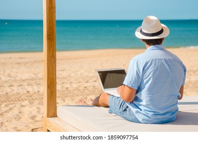 Back side view of telecommuting remotely businessman relaxing on the beach using laptop pc computer, education learning, teaching. Sun shining daytime natural blue sky background dream workplace - Shutterstock ID 1859097754
