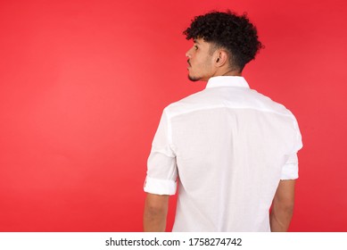 The back side view of a Young arab man with afro hair wearing shirt standing over isolated red background. Studio Shoot. - Powered by Shutterstock