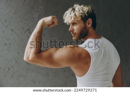 Back side view young calm strong sporty athletic sportsman man wearing white tank shirt showing biceps muscles on hand demonstrating strength power warm up training indoor at gym Workout sport concept
