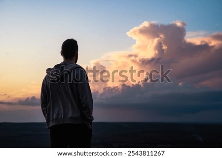Back side view of young man looks at the amazing sunset, guy standing looking and dreaming of future success, thinking of new goals, relaxing, feeling of freedom at sunset, travel holidays 