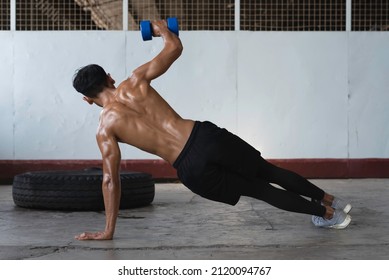 Back Side Of Young Man With Fit And Firm Muscle,sweat All Over His Body,Push-up With One Arm,lifting Dumbbell Up In The Air,blurry Light Around