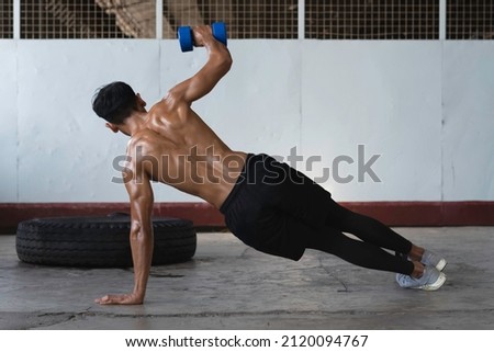 Back side of Young man with fit and firm muscle,sweat all over his body,Push-up with one arm,lifting dumbbell up in the air,blurry light around