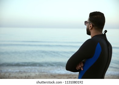Back side of young man looking at the sea, standing with his arms crossed.