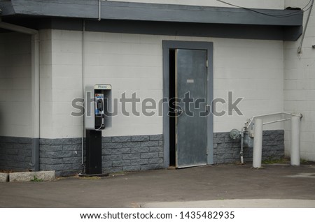 Back of small industrial Building with open Door, Payphone, and gas Pipes