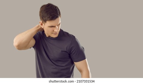 Back and spine disease. Young unhappy muscular man suffers from neckache due to muscle spasm or pinched nerve. Caucasian man in black T-shirt rubs his neck on gray background. Isolated. Banner.
