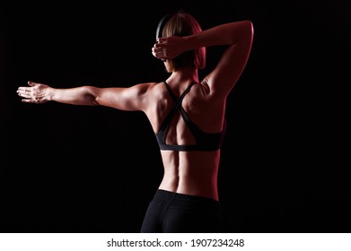 Back of sportswoman with muscular body stretching after workout. Slim girl listen music while training