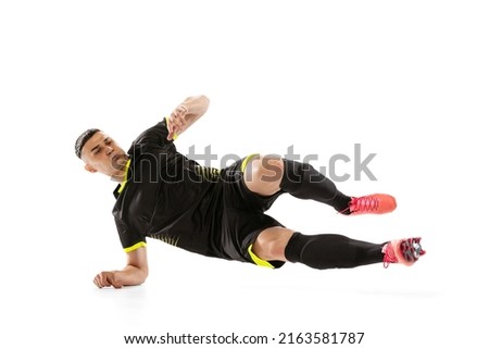 Back tackle. Professional male football soccer player doing sliding tackle isolated on white studio background. Concept of sport, goals, competition, hobby, ad. Sportsmen wearing black football kit