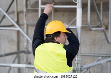 Back Turned Construction Worker Climbing A Ladder Up To The Scaffolding