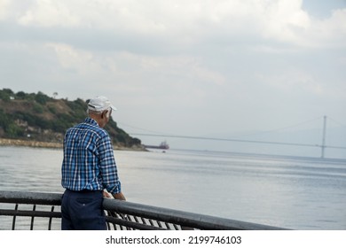 Back Turned Old Man Looking Forward And Trying To Fishing, Cinematic Scene, Older Man's Hobbies Idea, Calm And Relaxed Scene, Bridge And Mountain In The Background