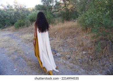 Back Turned Woman Walking In The Forest. The Woman Has A White Cloak And Long Black Hair.