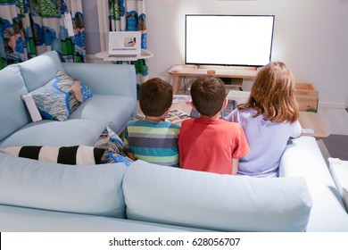 Back view of 3 children watching television in living room.