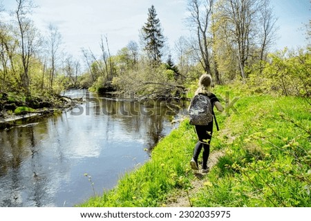 Back view of 9 year old girl hiking, walking alone in the forest by the river with a backpack in early spring. Beautiful idyllic nature.