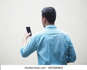 Back view of Adult Asian man wearing bright blue shirt looking to mobile phone screen. Isolated on white