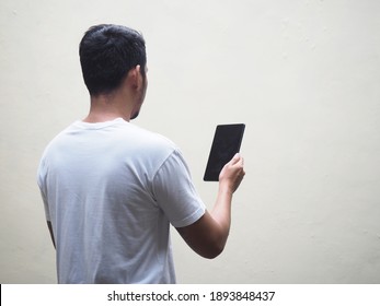 Back View Of Adult Asian Man Wearing White T-shirt Holding And Looking To Mobile Tablet. Isolated On White