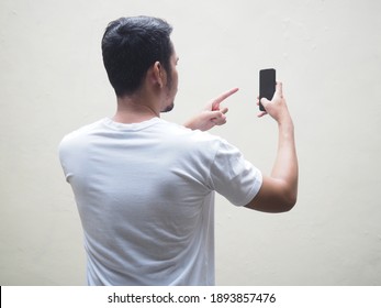 Back View Of Adult Asian Man Wearing White T-shirt Holding Mobile Phone And Pointing Finger To The Screen. Isolated On White