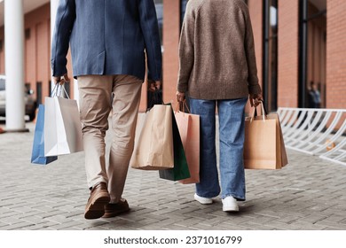 Back view of adult couple with shopping bags walking together outdoors by mall, copy space - Powered by Shutterstock