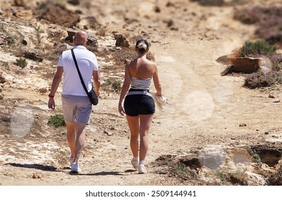 Back view of adult couple walking on rocky beach. Man and woman in shorts and t-shirt. - Powered by Shutterstock