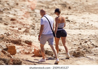 Back view of adult couple walking on rocky beach. Man and woman in shorts and t-shirt. - Powered by Shutterstock