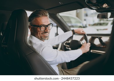 Back view adult man customer male buyer client wear shirt sit drive electric car look camera choose auto want to buy new automobile in showroom vehicle salon dealership store motor show. Sales concept - Powered by Shutterstock