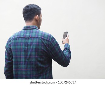 A Back View Of Adult Man Wearing Flannel Shirt Looking To The Mobile Phone Isolated On White. Space For Copy 