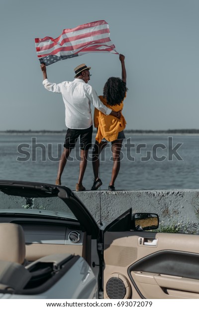 back view of african american couple\
with american flag standing on parapet\
together