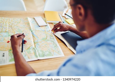 Back View Of African American Hipster Guy Looking At Topographic Map Learning At Desktop, Cropped Image Of Dark Skinned Man Planning Journey Using Map Checking Routes And Destination For Traveling