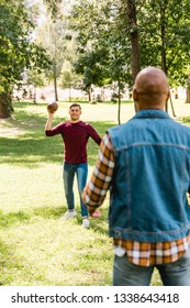 Back View Of African American Man Looking At Happy Friend Throwing American Football In Park