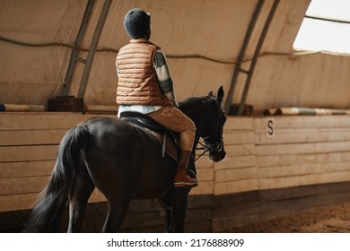 Back view of African American woman riding horse in indoor arena at horse ranch or practice stadium, copy space - Powered by Shutterstock