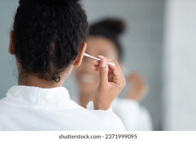 Back view of african American woman look in mirror clean cleanse ears with cotton bud or stick in bathroom, biracial girl take care of body hygiene, do daily beauty procedures in home bath - Powered by Shutterstock