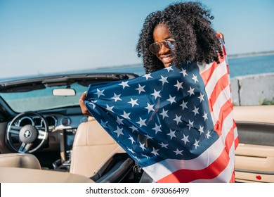 back view of african american woman with american flag sitting in car at seaside - Powered by Shutterstock