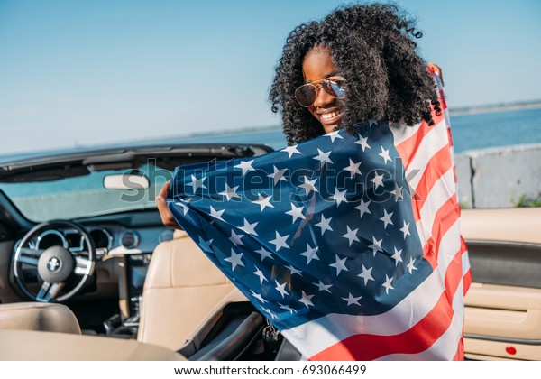 back view of african american woman with american\
flag sitting in car at\
seaside