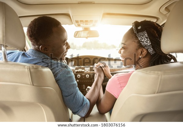Back view of african couple holding hands in\
car, traveling together