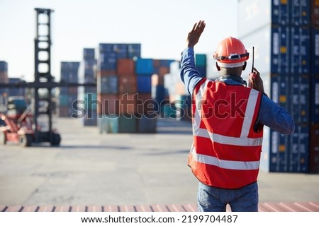 back view African factory worker or engineer using walkie talkie and showing stop gesture to crane car in containers warehouse storage