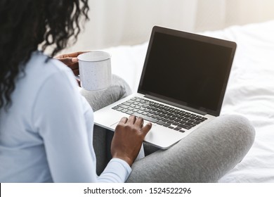 Back View Of African Girl Looking At Blank Laptop Screen, Sitting On Bed, Drinking Tea, Cropped