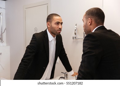 Back view of African man in suit looking at mirror in bathroom in hotel room