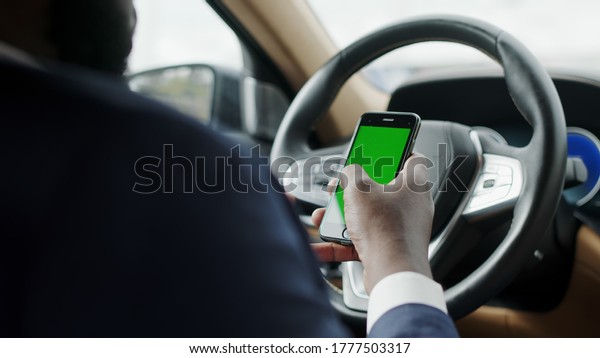 Back view\
african man using mobile phone with green screen at car. Black\
businessman typing smartphone at vehicle. Stylish african american\
professional sitting with phone at\
automobile.