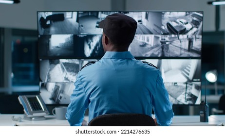 Back view of African-American security operator use computer with screens showing surveillance camera footage . 