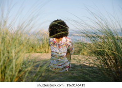 Back View Of Afro Hairstyle Black Woman Relaxing At The Beach On Summer Or Spring Vacation.