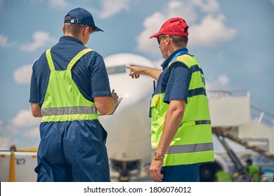 Back view of an aircraft maintenance engineer pointing at the parked plane to his colleague