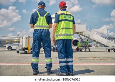 Back view of an aircraft maintenance supervisor and his colleague standing in front of the plane